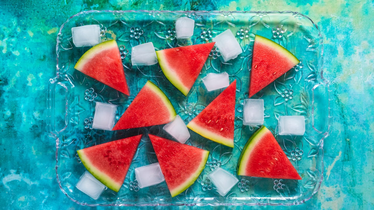Rebanadas de sandía en una bandeja de vidrio con cubitos de hielo como un postre de verano sobre un fondo verde
