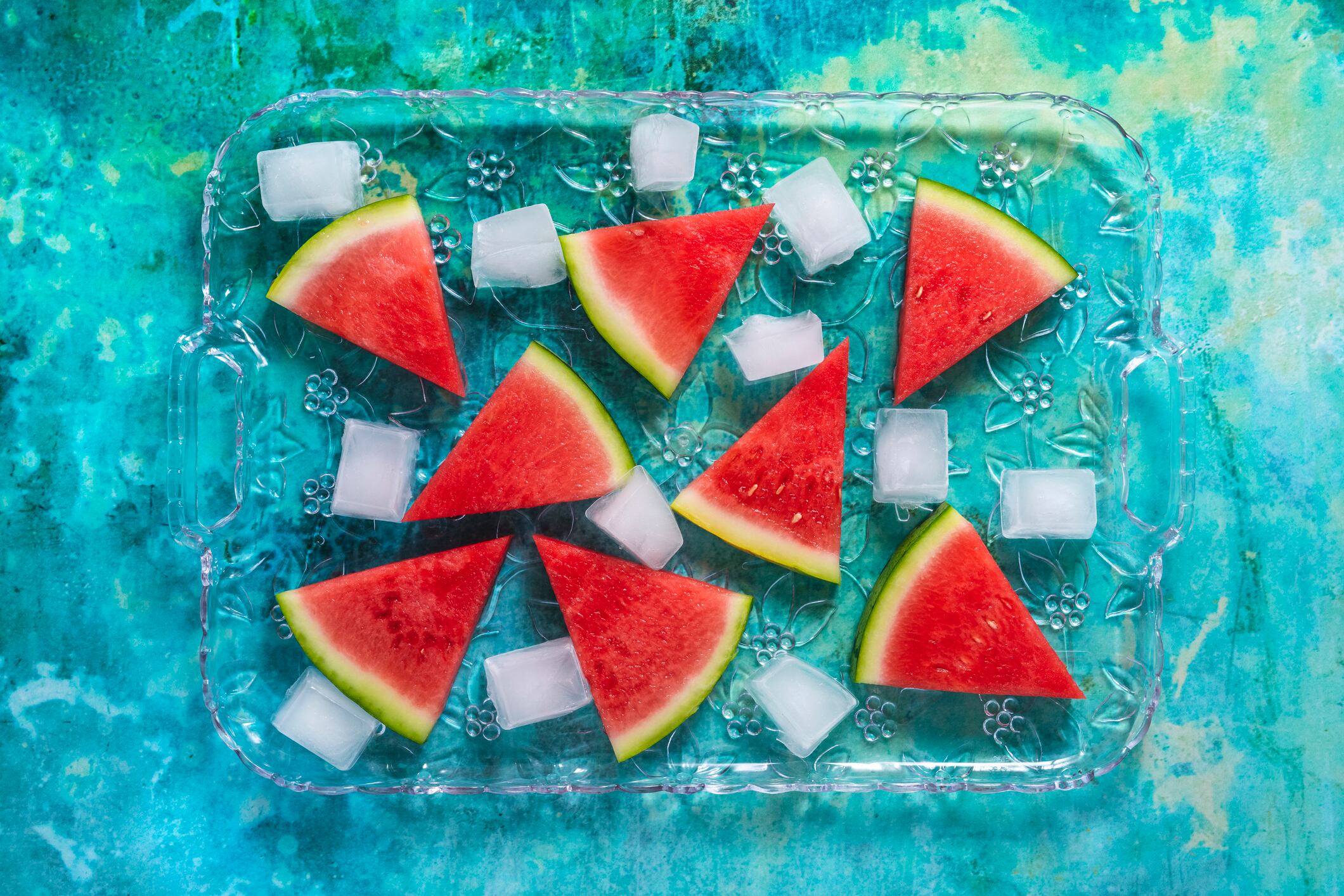 Rebanadas de sandía en una bandeja de vidrio con cubitos de hielo como un postre de verano sobre un fondo verde