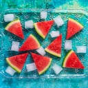 Rebanadas de sandía en una bandeja de vidrio con cubitos de hielo como un postre de verano sobre un fondo verde