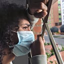 Latin man with frizzy hair and dark skin of approximately 20 years old is leaning out of the window of his house. He uses his protection mask to avoid viruses on his face. We observe a feeling of despair at the quarantine that they are going through because of the covid 19