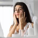 Anti-Wrinkle Skincare. Sad Young Woman Touching Face Looking At Her Skin In Mirror At Bathroom. Selective Focus, Panorama