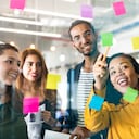 Jóvenes profesionales que planean tareas en una pared de vidrio con notas adhesivas en una oficina de trabajo conjunto