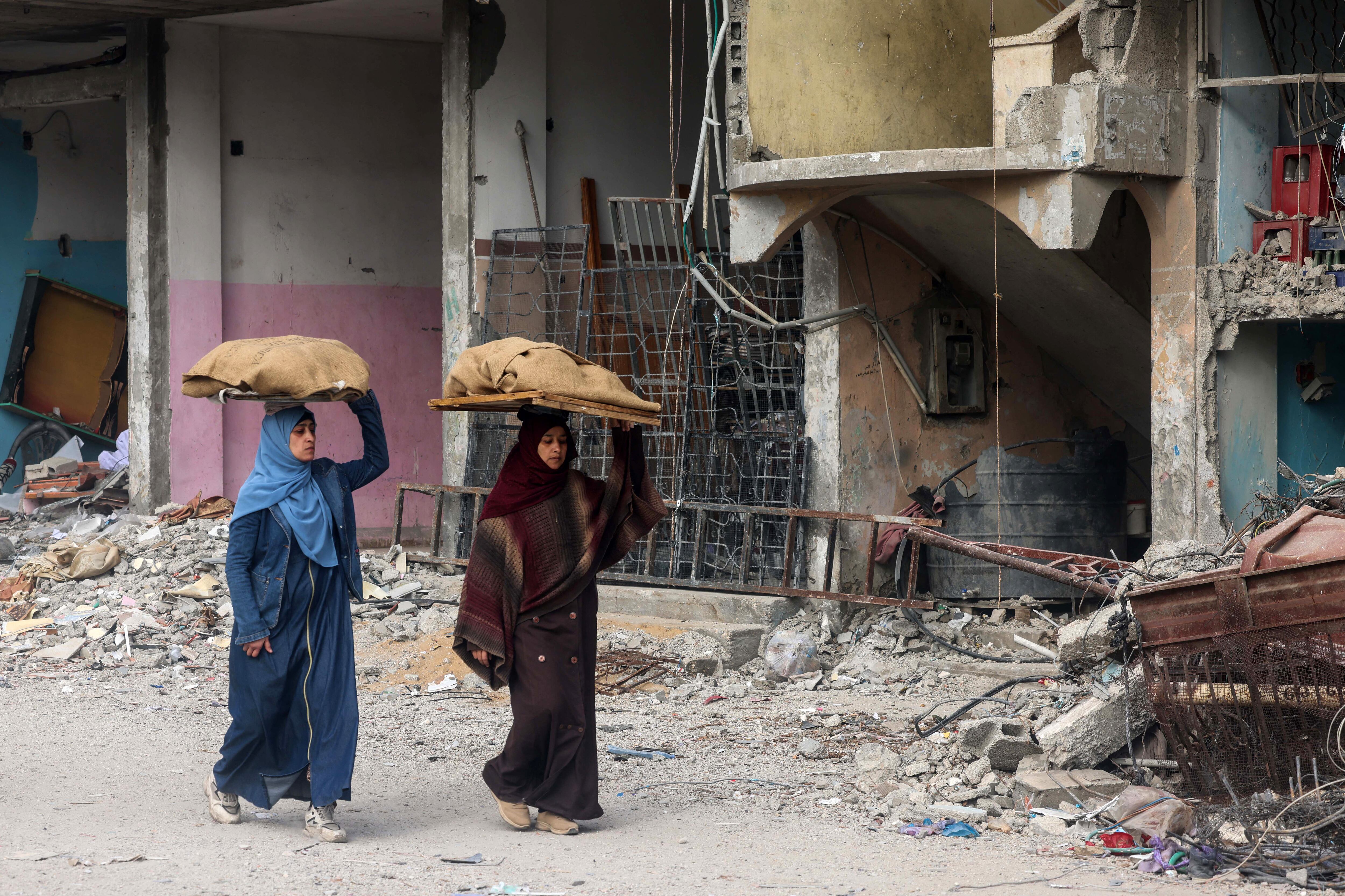 Las mujeres llevan hogazas de pan sobre sus cabezas mientras caminan frente a un edificio dañado por el bombardeo israelí en Rafah, en el sur de la Franja de Gaza, el 25 de febrero de 2024, en medio de continuas batallas entre Israel y el grupo militante palestino Hamas. (Foto de MOHAMMED ABED / AFP)