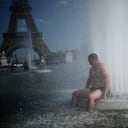 Una persona se refresca en la fuente del Trocadero, cerca de la Torre Eiffel, durante una ola de calor en París.