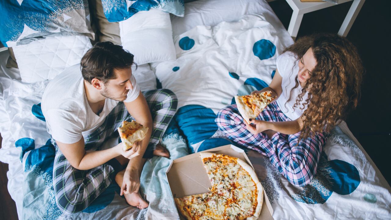 Una pareja comiendo pizza en una cama