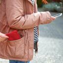 Cerca de una mano robando un bolso del bolsillo de una niña mientras ella está distraída en su teléfono