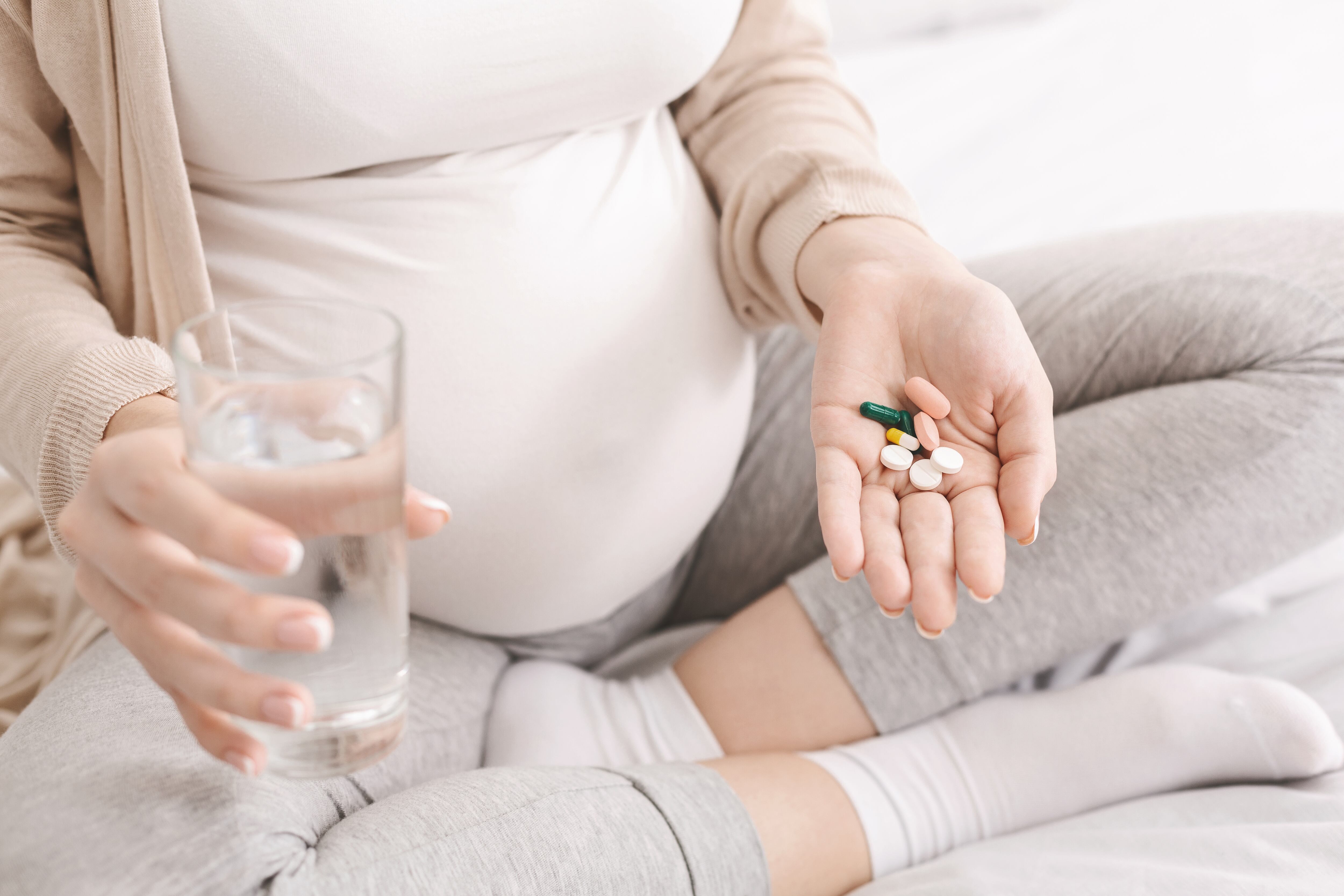 Vitamins for pregnant Expectant woman holding bunch of pills and glass of water, closeup