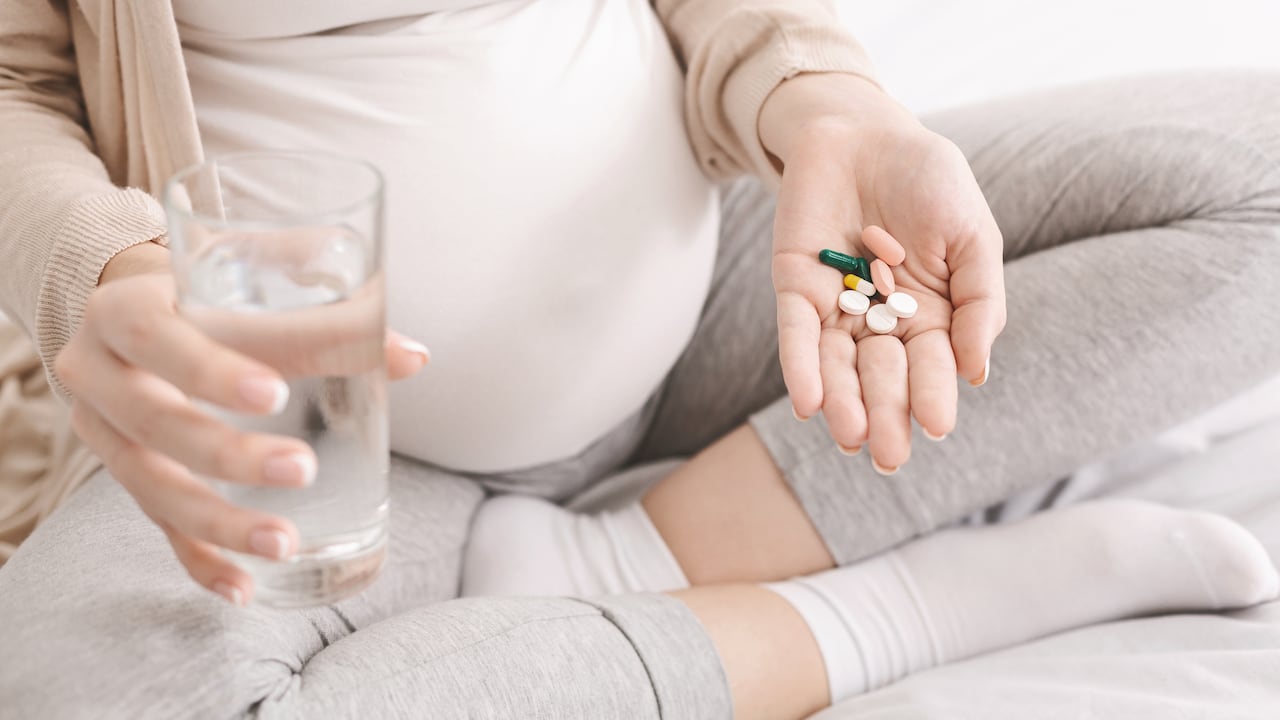 Vitamins for pregnant Expectant woman holding bunch of pills and glass of water, closeup
