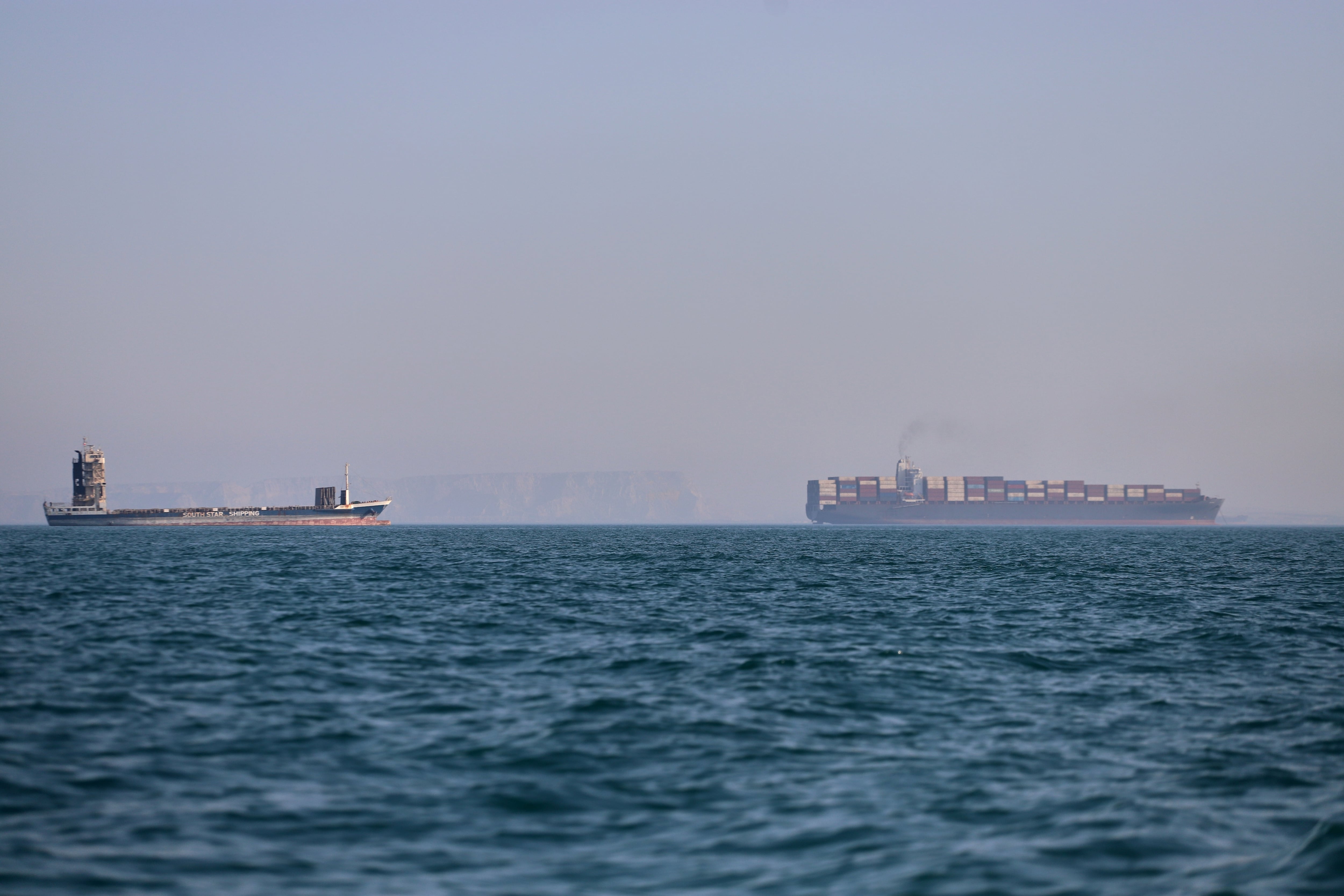Un buque portacontenedores (a la derecha) y otro barco de carga pueden apreciarse en el estrecho de Ormuz, frente a Bandar Abbas, Irán.