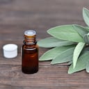 Salvia officinalis herb and sage essential oil in a bottle on a wooden table.