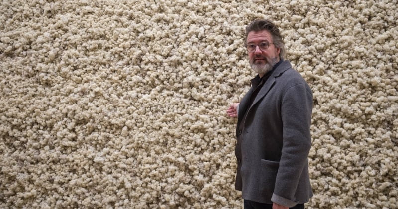 El artista Olafur Eliasson aparece parado frente a una pared de un material corrugado.