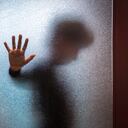 Niño triste y borroso apoyado con la mano abierta contra la puerta de cristal.