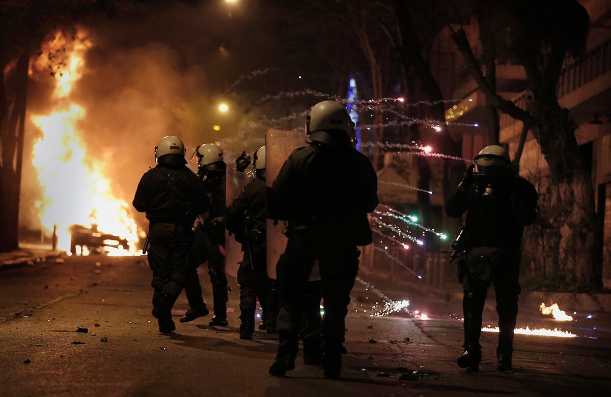 La policía antidisturbios griega se refugia de una bengala lanzada por los jóvenes que protestan para exigir la abolición de una prisión de máxima seguridad. (AP)