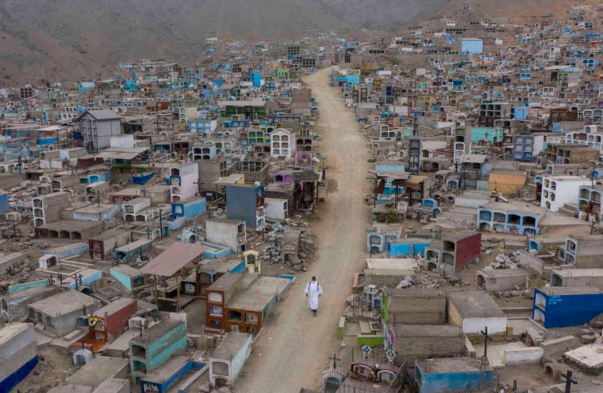 El hermano Ronald Marín, un trabajador laico venezolano de 30 años, va por un camino de tierra bordeado de tumbas, dentro del cementerio Mártires 19 de Julio en Comas, a las afueras de Lima, Perú. Imagen del sábado 4 de julio de 2020. Con una túnica blanca y zapatos desgastados por el polvo, Marín es uno de los pocos que administra los funerales en este cementerio lejos del centro de la capital de Perú. Foto: Rodrigo Abd / AP