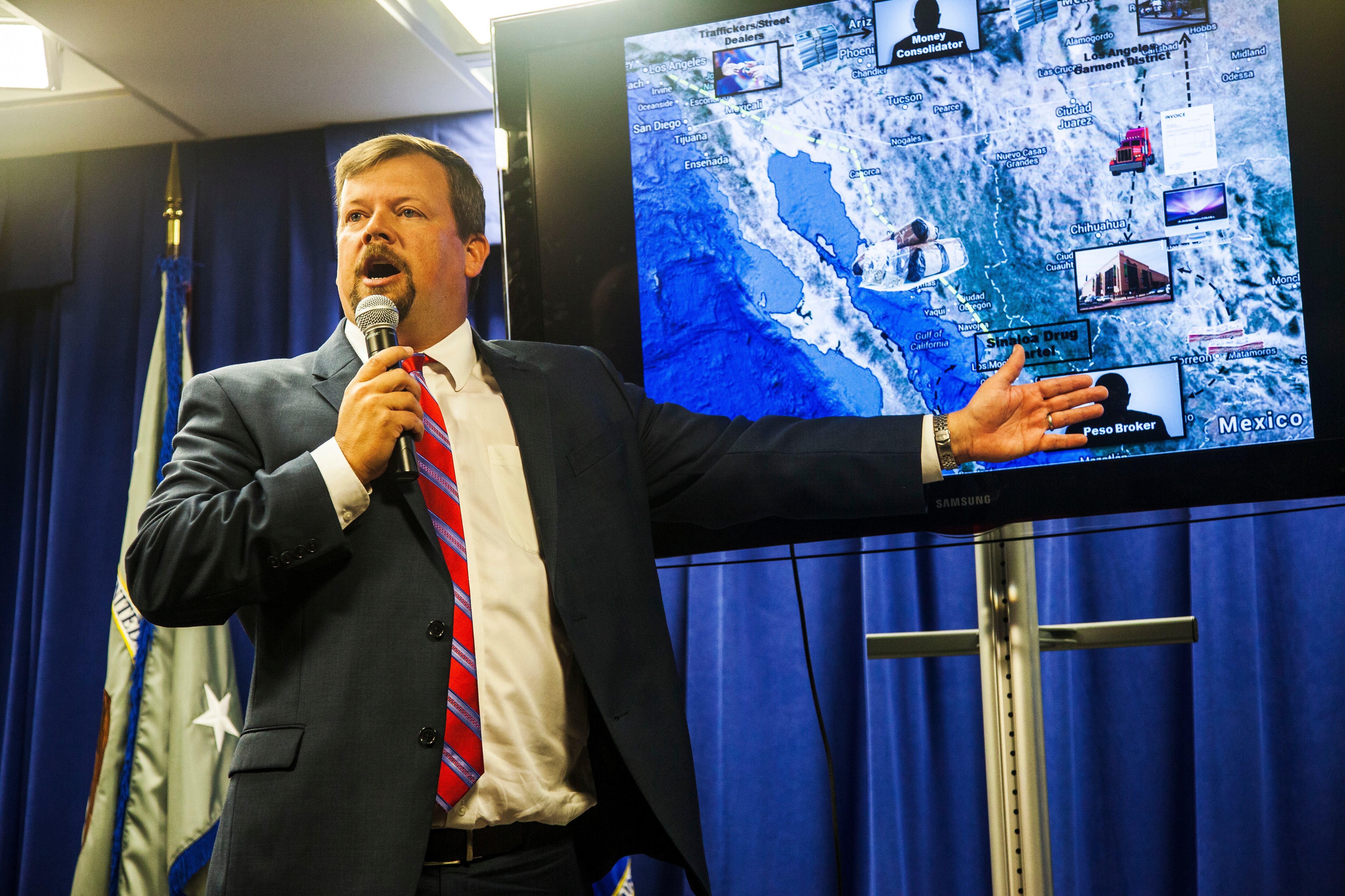 Robert E. Dugdale, Fiscal Federal Auxiliar, Jefe de la División Penal, con una captura de pantalla del plan de lavado de dinero "Peso Negro". Conferencia de prensa en el Edificio Federal de Los Ángeles para anunciar una redada multigubernamental y de agencias policiales en negocios del centro de Los Ángeles vinculados con muchos lavados para los cárteles de la droga. Más de 1000 agentes del orden entregaron órdenes de búsqueda y arresto a empresas sospechosas de utilizar esquemas de "mercado negro de cambio de pesos" para lavar dinero para la droga de Sinaloa