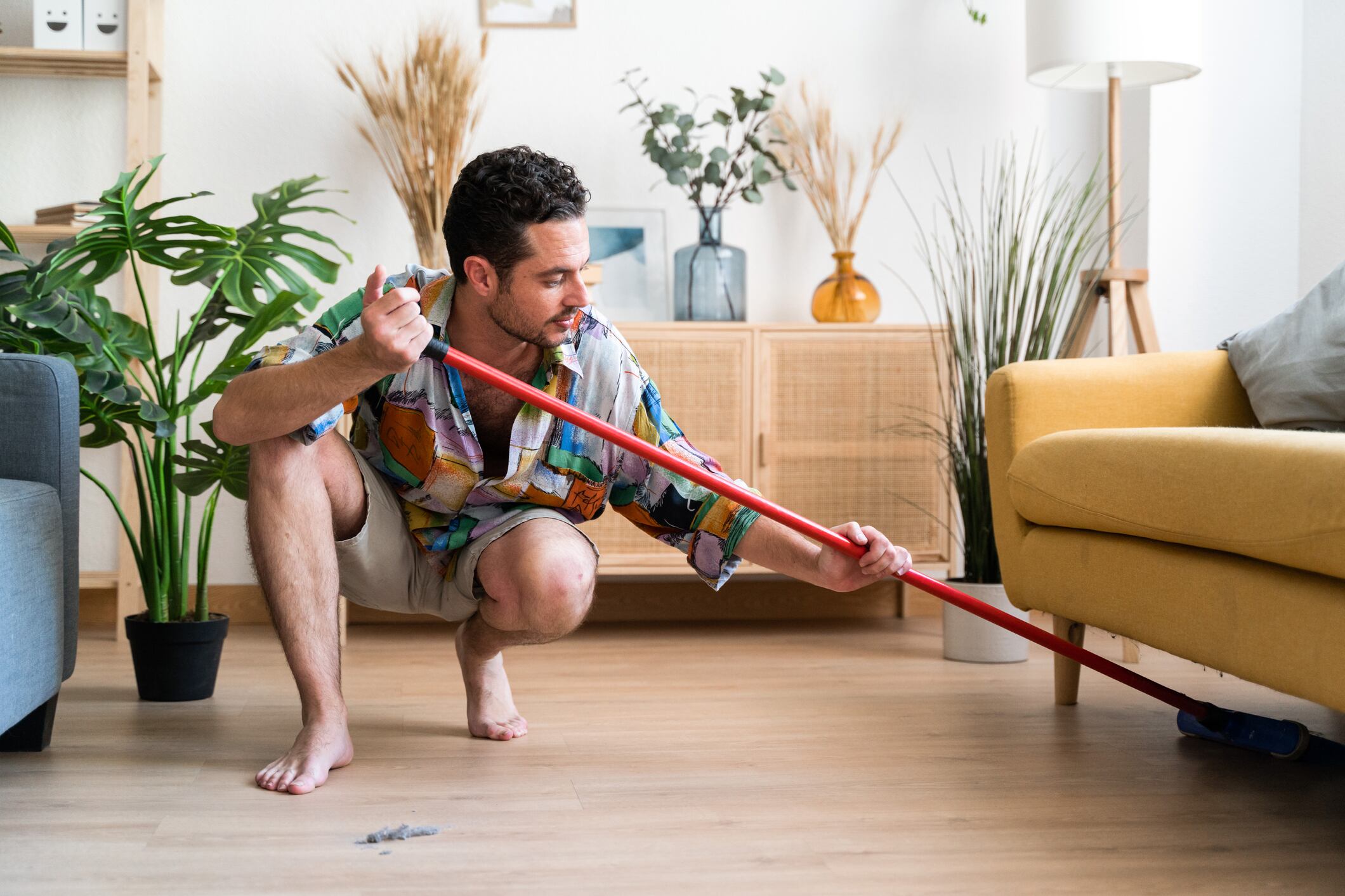 Man cleaning the floor of the living room of his house with a broom.