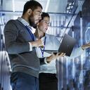 Male IT Specialist Holds Laptop and Discusses Work with Female Server Technician. They're Standing in Data Center, Rack Server Cabinet with Cloud Server Icon and Visualization.