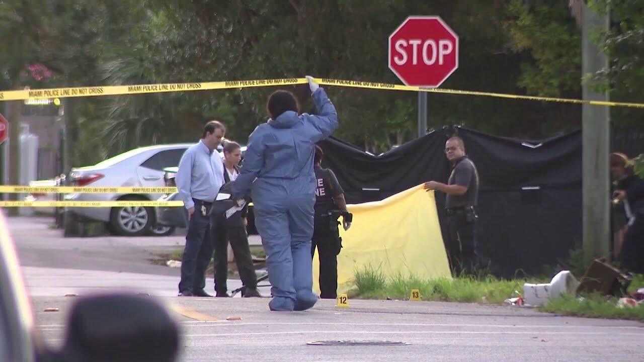 Investigadores recogen pruebas balísticas en la escena del crimen mientras los vecinos observan desde la acera