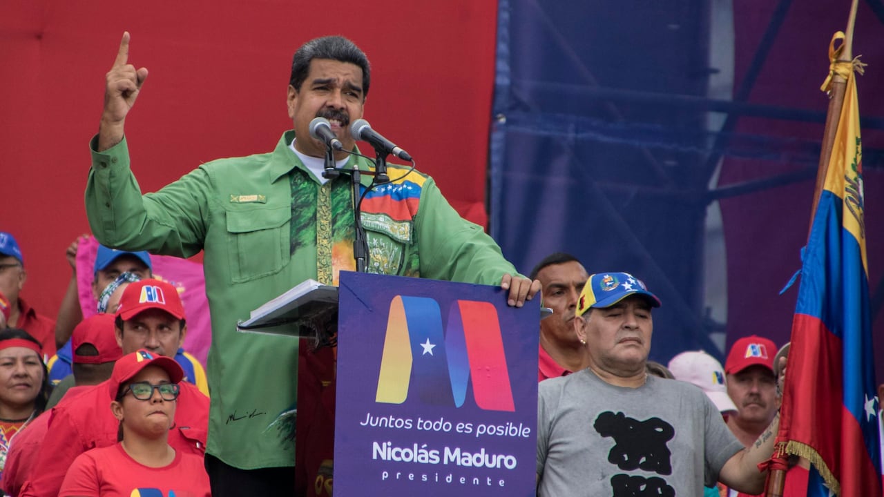 la ex estrella del fútbol argentino Diego Maradona (R) sostiene la bandera venezolana mientras el presidente venezolano, Nicolás Maduro, pronuncia su último discurso de campaña.