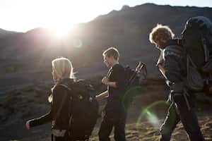 Tres mochileros caminando en zona de montaña.