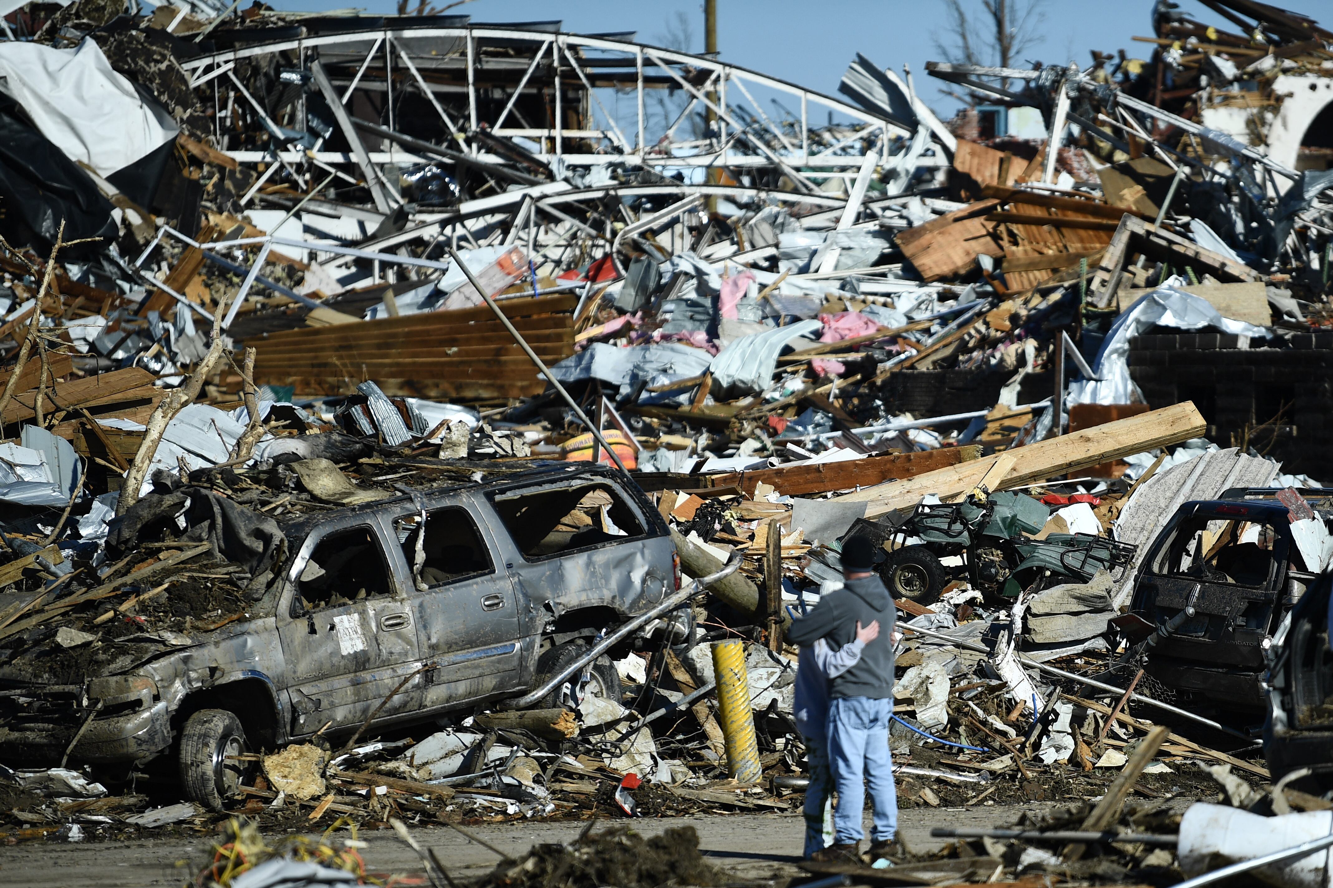 People embrace as tornado damage is seen after extreme weather hit the region December 12, 2021, in Mayfield, Kentucky. - Dozens of devastating tornadoes roared through five US states overnight, leaving more than 80 people dead Saturday in what President Joe Biden said was "one of the largest" storm outbreaks in history. (Photo by Brendan Smialowski / AFP)