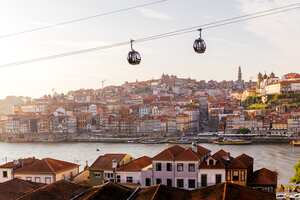 Cabinas de teleférico moviéndose sobre la ciudad de Oporto y el río Duero al atardecer, Portugal