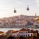 Cabinas de teleférico moviéndose sobre la ciudad de Oporto y el río Duero al atardecer, Portugal