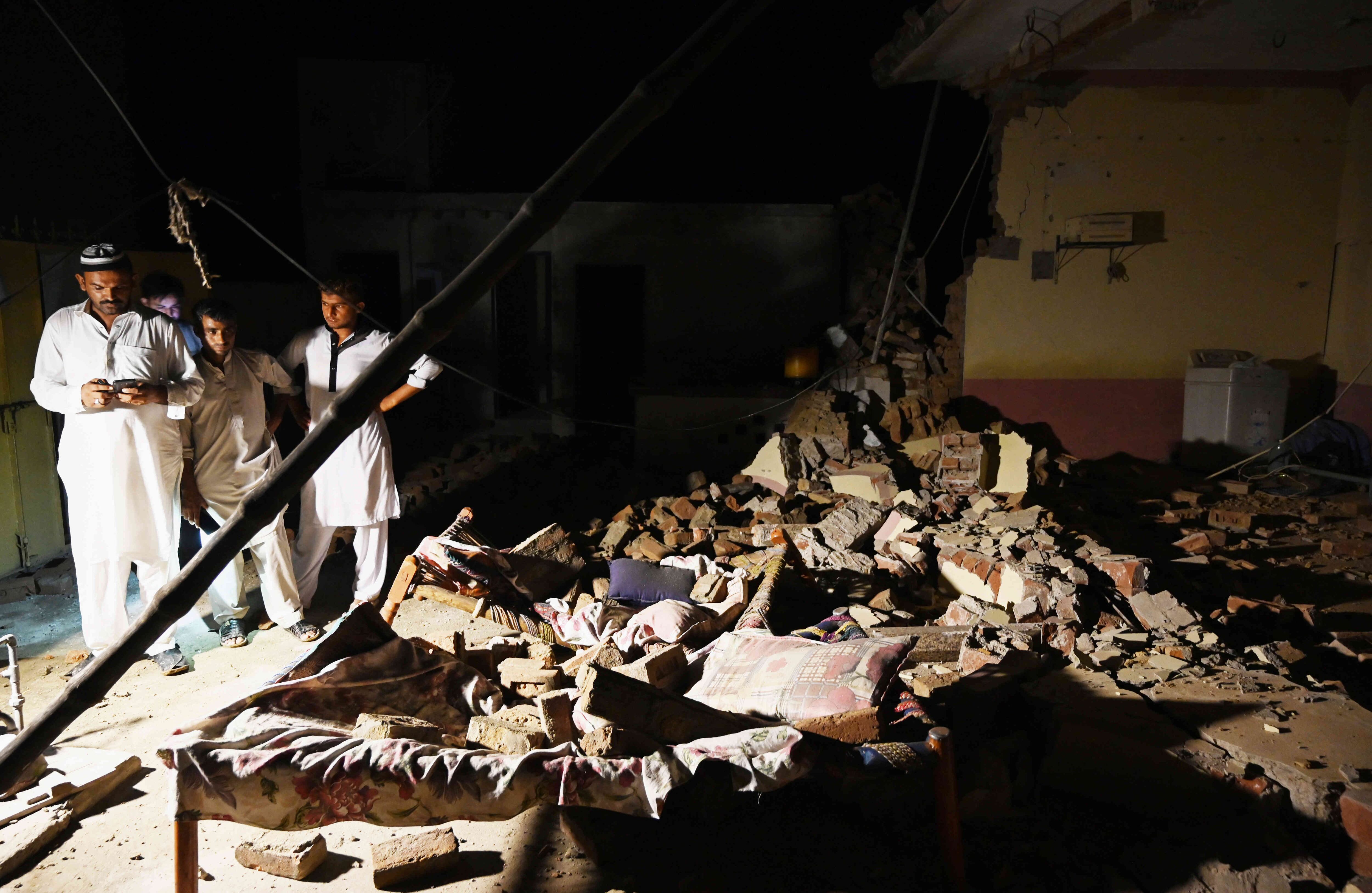 Tres hombres buscan a sus allegados entre los escombros de una de las estructuras que colapsó debido al terremoto. Foto: AFP/ AAMIR QURESHI.