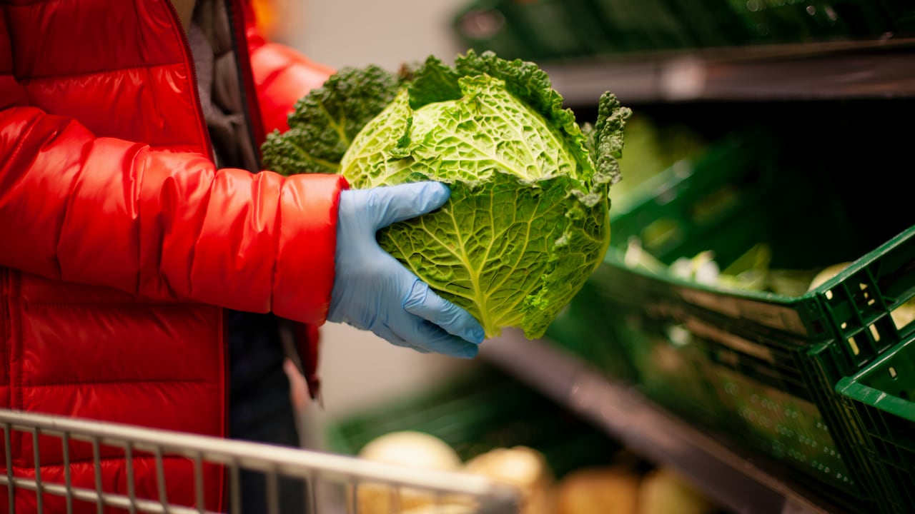 Mujer recogiendo col de col rizada en el supermercado, con guantes de protección