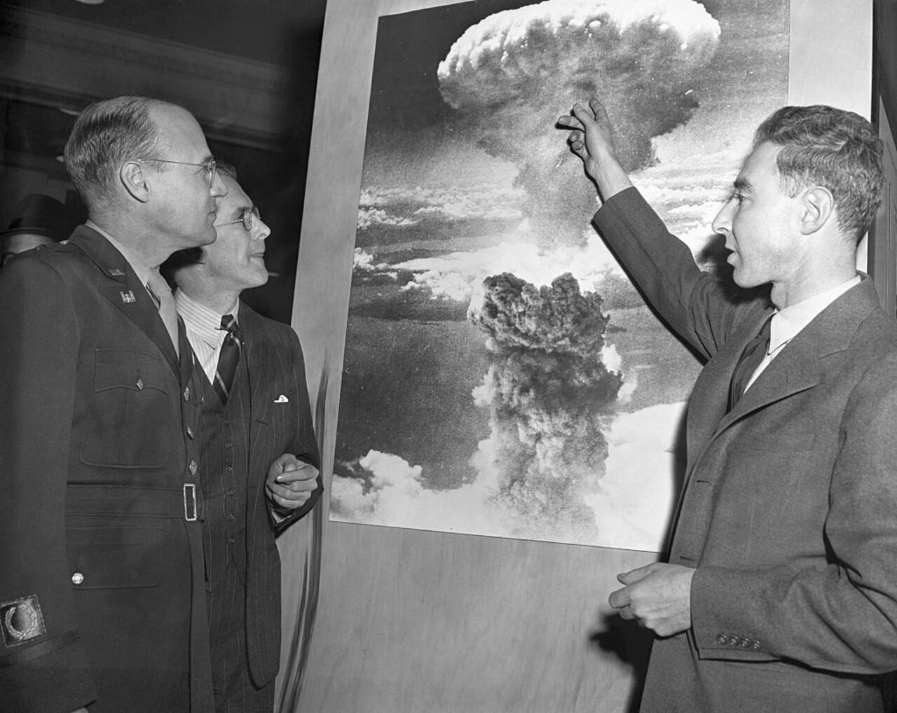 Tres de los hombres que desempeñaron papeles destacados en el desarrollo de la bomba atómica visitan la exposición atómica de la Sociedad Química Estadounidense en el Grand Central Palace. Mirando una foto de la explosión atómica sobre Nagasaki, Japón, de izquierda a derecha, Brig. Gen. K. D. Nichols, Prof. H.D. Smythe, quien escribió el informe atómico del gobierno y J.R. Oppenheimer, director del laboratorio atómico de Los Alamos, Nuevo México.