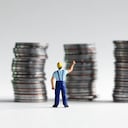 Un hombre en miniatura que alcanza una pila de tres monedas.