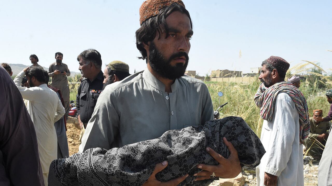 A man carries the body of his child, who was killed after a roof of a house collapsed, as he arrives for a burial following an earthquake in the remote mountainous district of Harnai on October 7, 2021, as around 20 people were killed and more than 200 injured when a shallow earthquake hit southwestern Pakistan in the early hours of October 7. (Photo by Banaras KHAN / AFP)