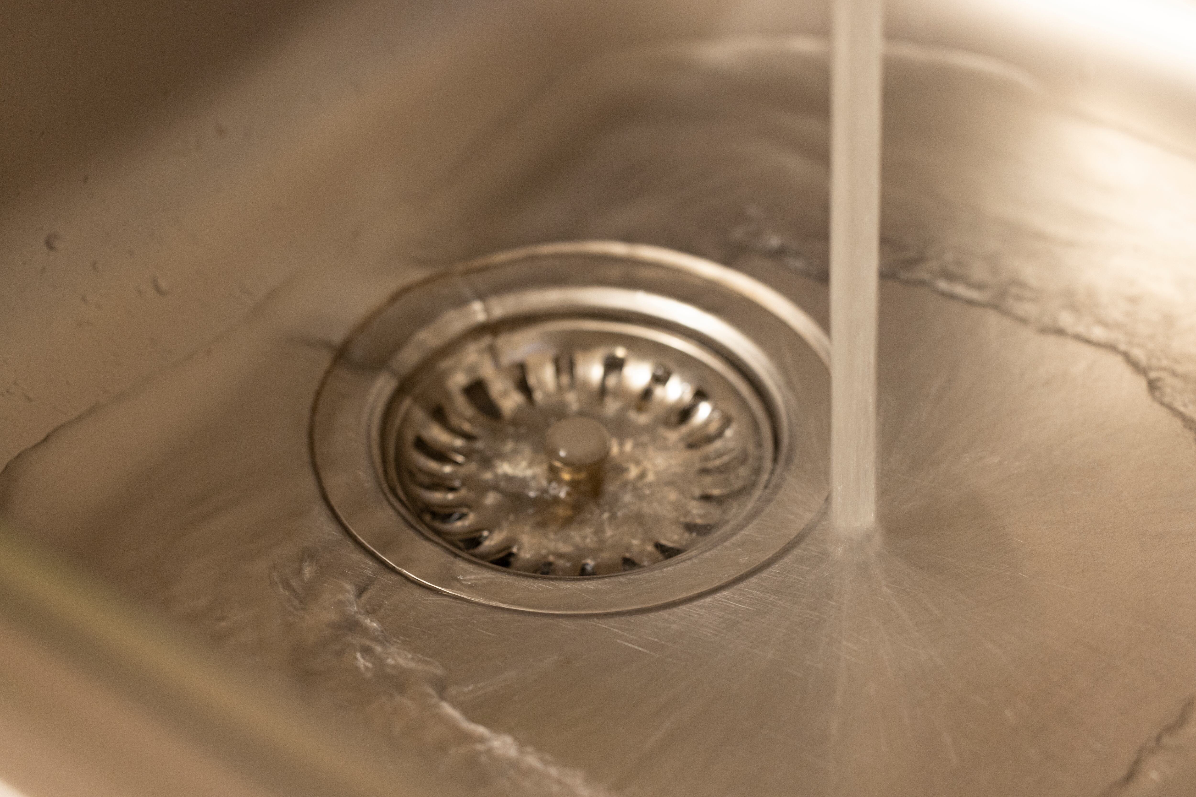 Primer plano de un orificio de desagüe de un lavaplatos de cocina con agua saliendo.