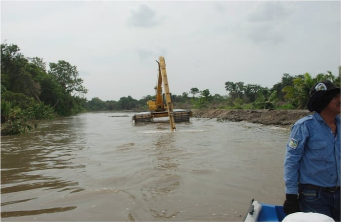 Retroescabadora del Banco de Maquinaría extrae lodo del río para construir un dique.