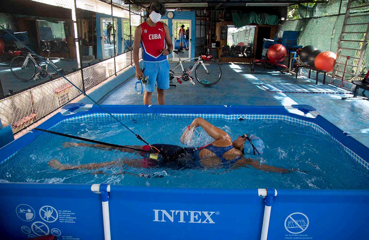 Leslie Amat, la atleta cubana de triatlón, nada bajo la mirada de su entrenadora Dioseles Fernández, en el patio de su casa, en La Habana, Cuba. Foto del 20 de abril. Amat se prepara para clasificar a los Juegos Olímpicos de Tokio 2021. Y debido a la cuarentena los hace con equipos improvisados que le ayudan a entrenar en interiores. Foto: Ismael Francisco/ AP