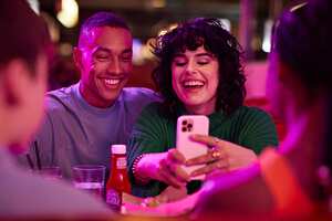 Cheerful woman taking selfie with man on smart phone by friends at bowling alley
