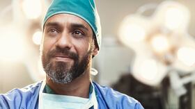 Cirujano de sexo masculino barbudo mirando a otro lado. El doctor está trabajando en quirófano iluminado. Lleva uniformes médicos.