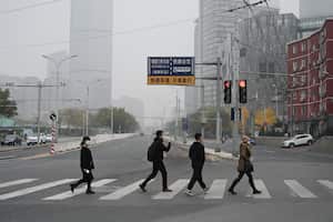 People cross a road in Beijing on November 5, 2021, after highways and school playgrounds were closed due to heavy pollution. (Photo by GREG BAKER / AFP)