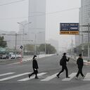 People cross a road in Beijing on November 5, 2021, after highways and school playgrounds were closed due to heavy pollution. (Photo by GREG BAKER / AFP)