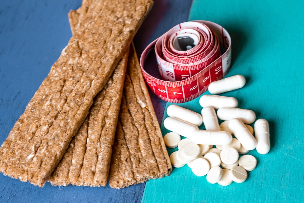 Panes de grano, pastillas adelgazantes y cinta métrica cinta métrica para el tamaño de la cintura yacen sobre una superficie de madera brillante como símbolo de delgadez y fitness