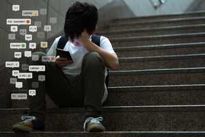 Asian teenage boy sitting at stair at school, covering his face with hands, face down, holding smartphone in low light feeling frustrated, lonely, stress and depressed. Cyber bullying concept.