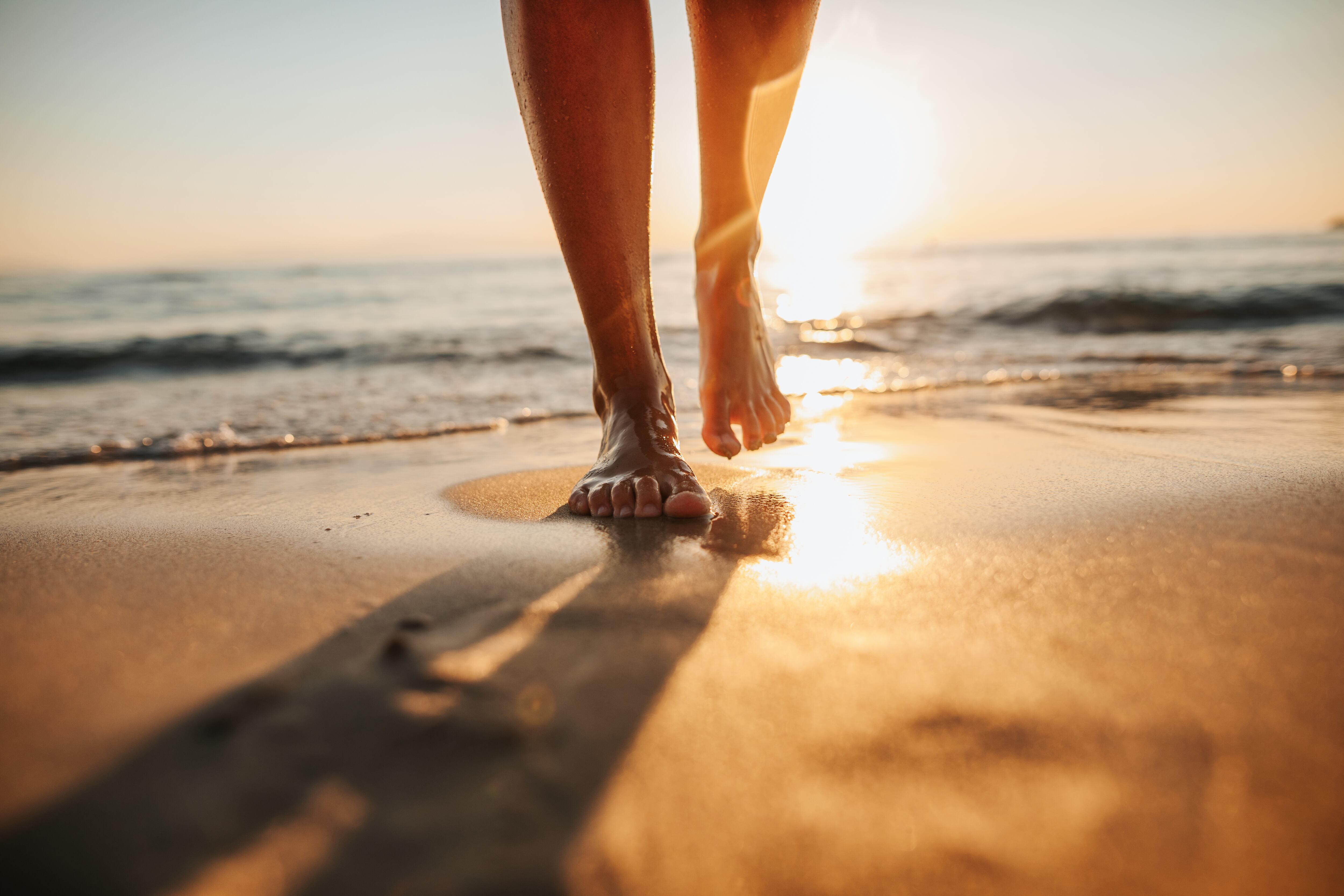 Close-up of female legs getting out of the sea water and walking on sandy beach at beautiful sunset