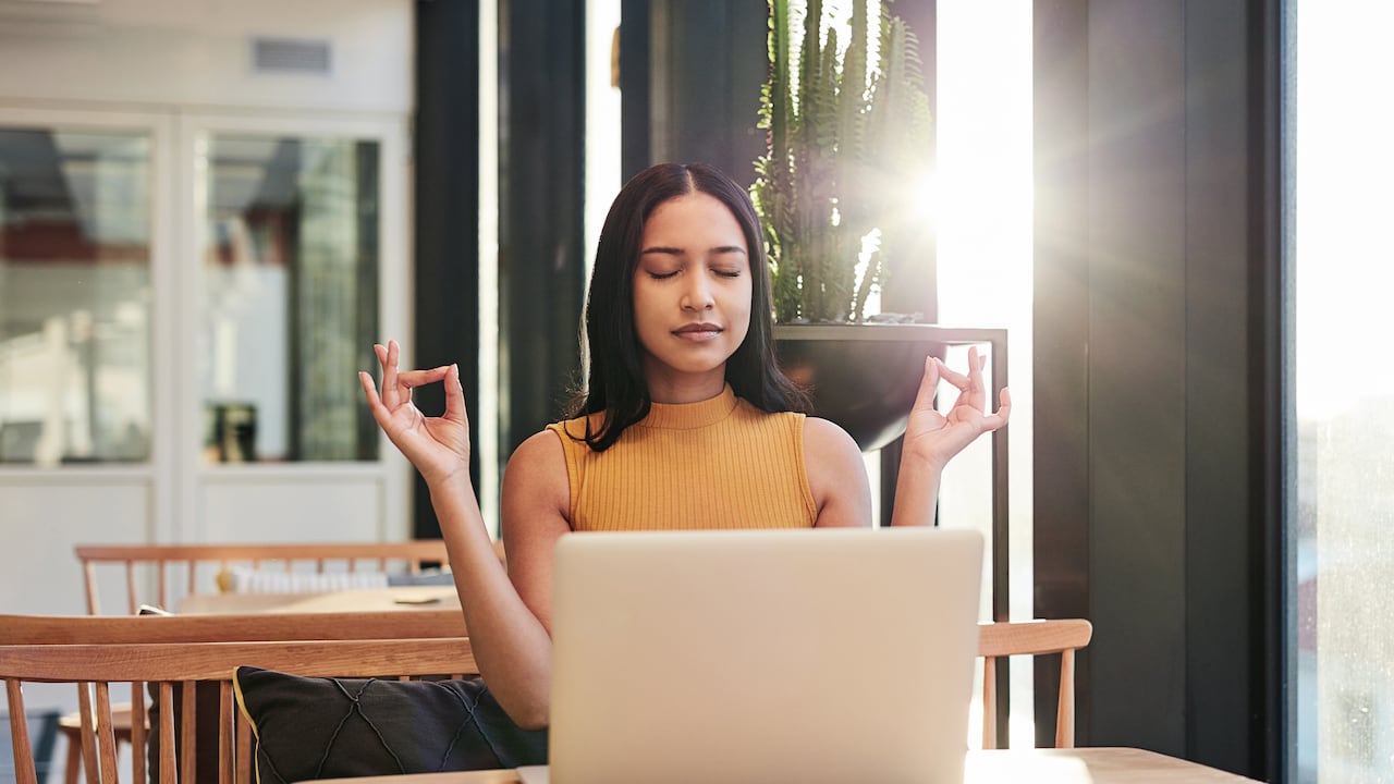Shot of a young businesswoman meditating while using a laptop in a modern office