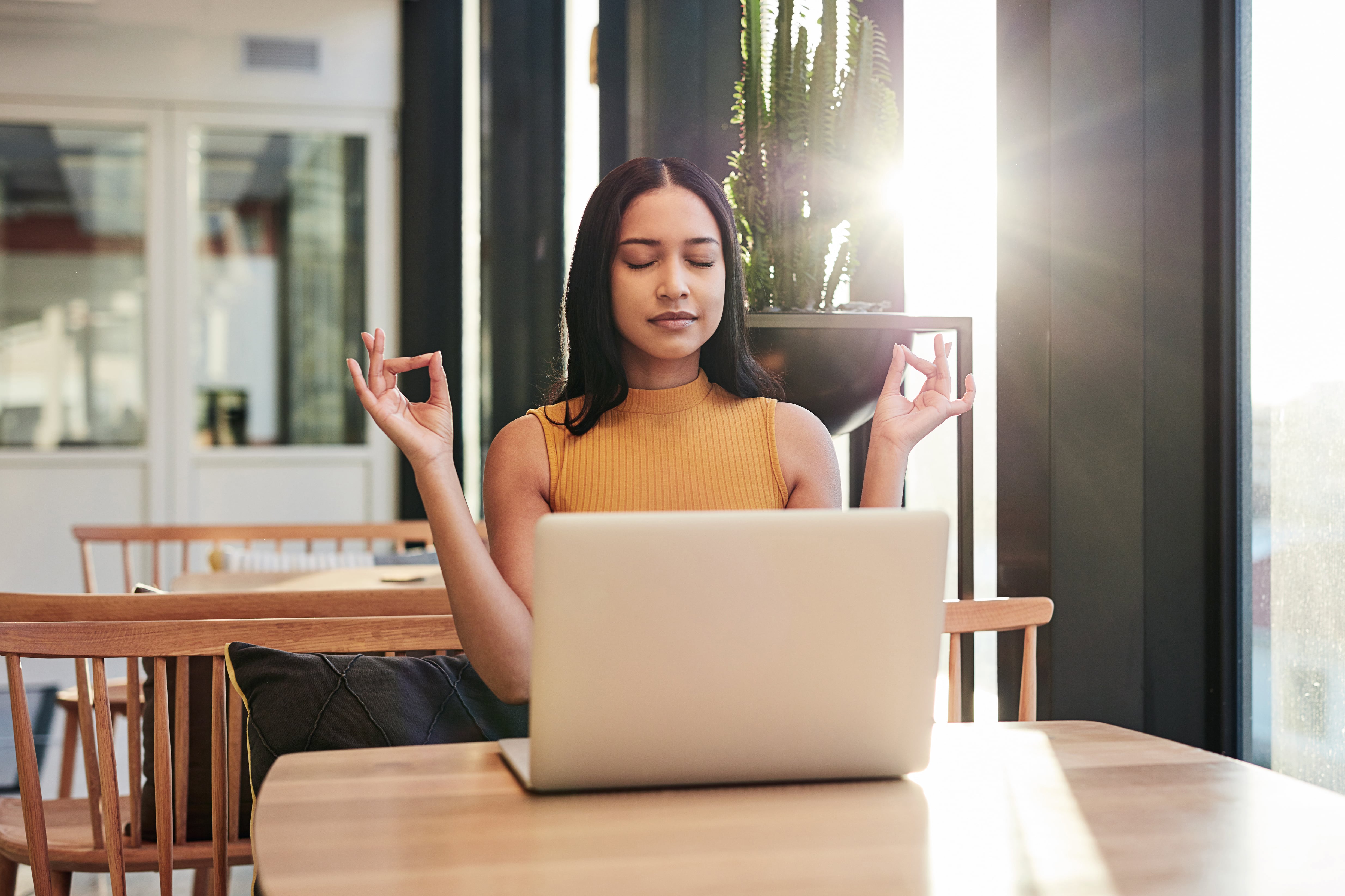 Shot of a young businesswoman meditating while using a laptop in a modern office