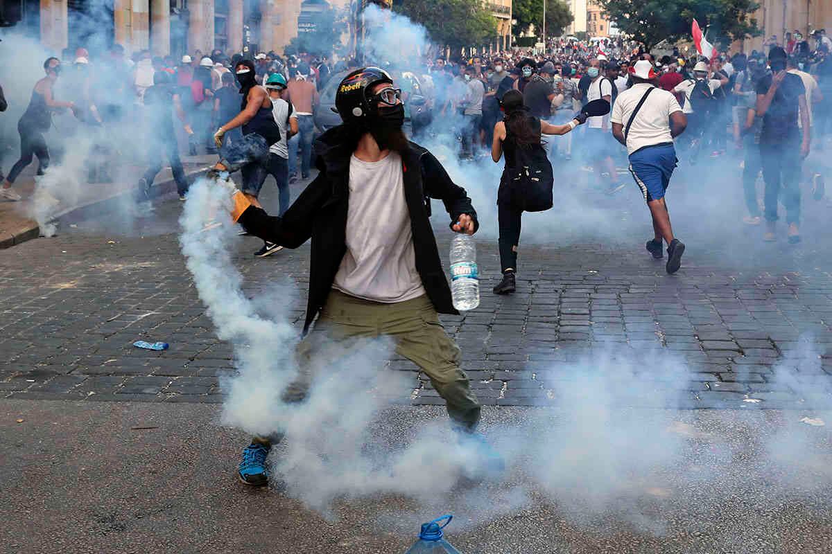 Los manifestantes arrojan gas lacrimógeno hacia los policías antidisturbios durante una protesta contra el gobierno, a raíz de la explosión masiva del martes pasado que devastó Beirut.  AP Photo/Bilal Hussein.