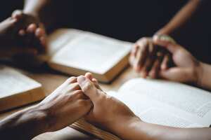 Christian group of people holding hands praying worship to believe and Bible on a wooden table for devotional or prayer meeting concept.