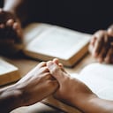 Christian group of people holding hands praying worship to believe and Bible on a wooden table for devotional or prayer meeting concept.