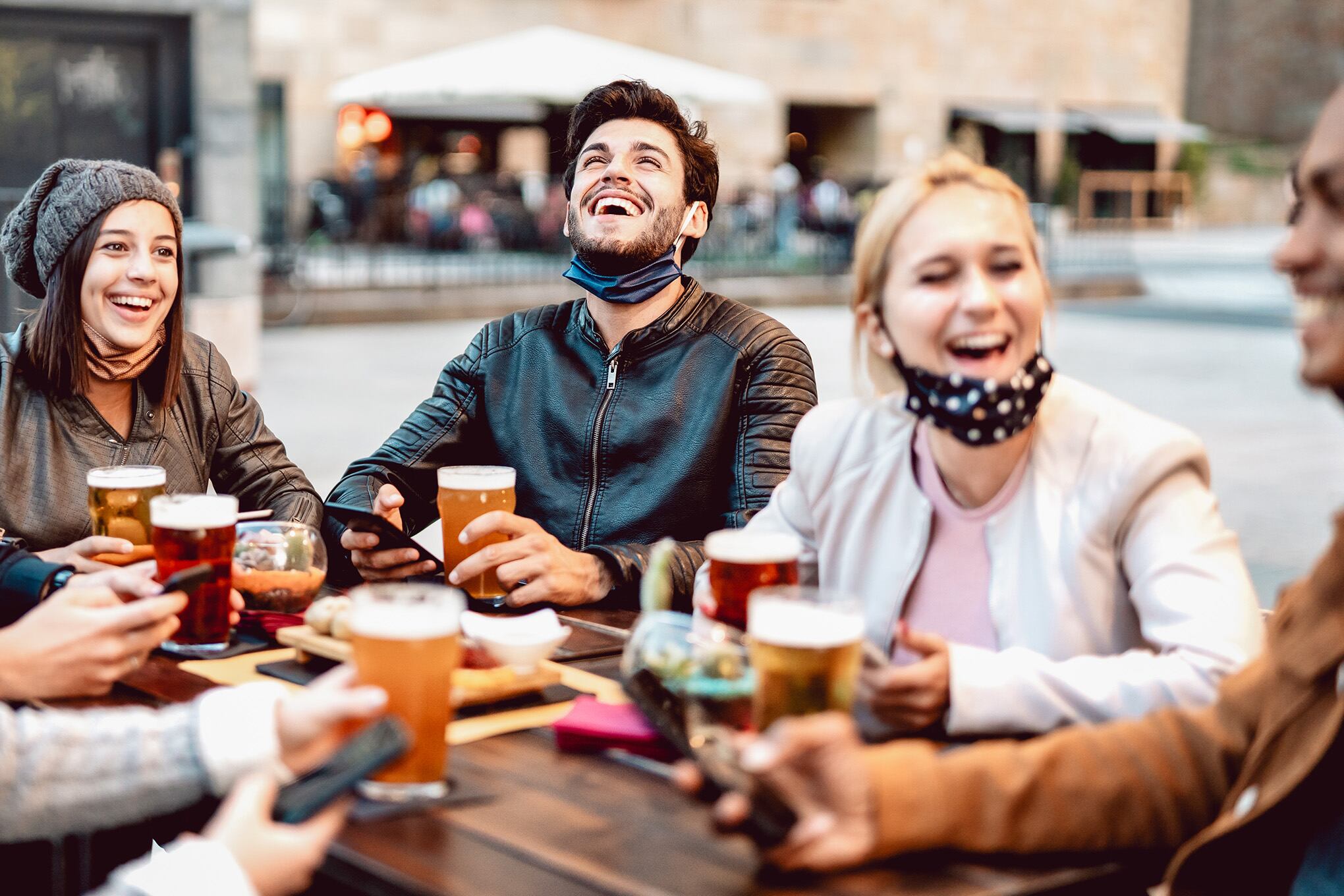Amigos jóvenes bebiendo cerveza con máscara facial - nuevo concepto de estilo de vida normal con gente que se divierte juntos hablando en la hora feliz en la barra de cervecería exterior - Filtro cálido brillante con enfoque en el centro central