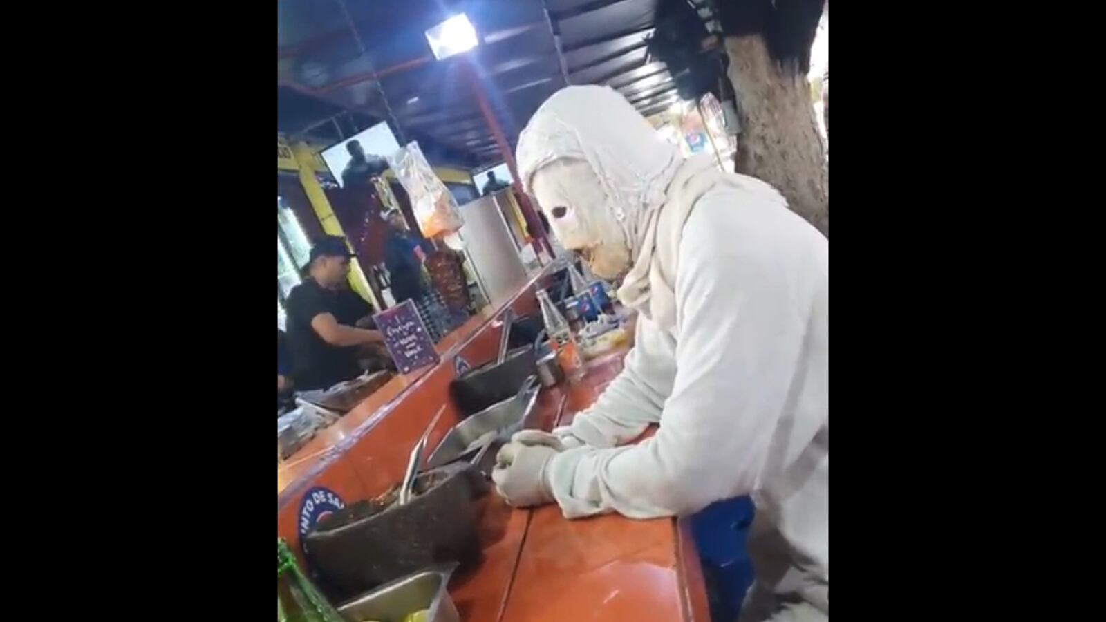 El hombre viste de blanco enteramente y tiene puesta una máscara de yeso.