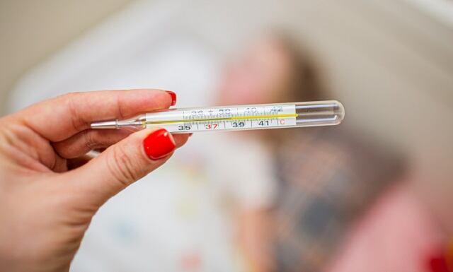 Womans hand holding mercury thermometer on the background of a sick child.